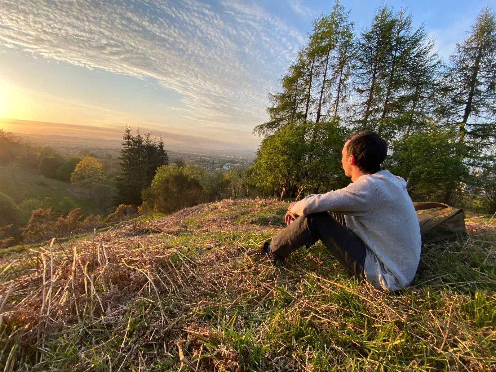 Connor sitting on a hillside at sunset, looking out over the landscape.